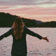 Woman standing infront of a lake with open hands