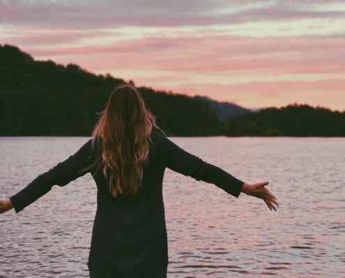 Woman standing infront of a lake with open hands