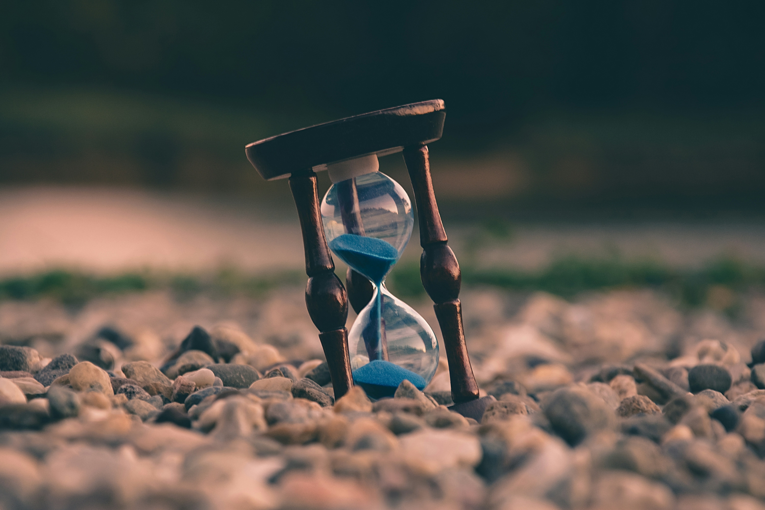 An hourglass resting on stones with sand running through it