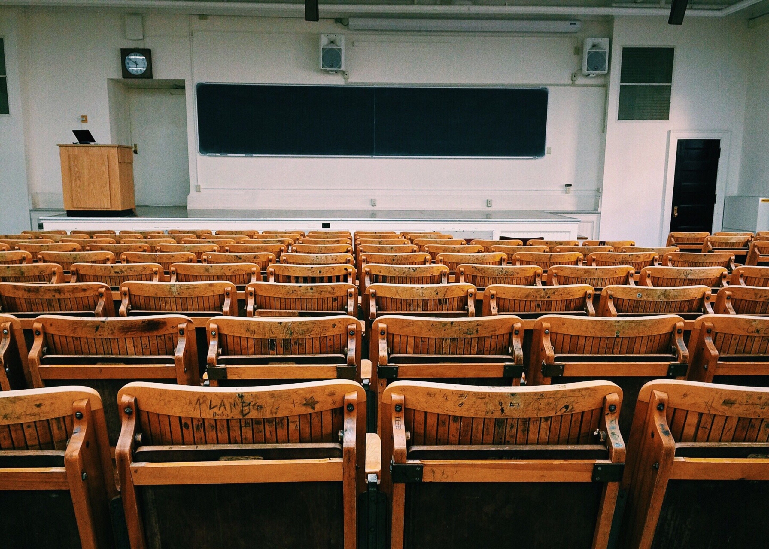 An empty lecture hall with wooden chairs facing a large blackboard