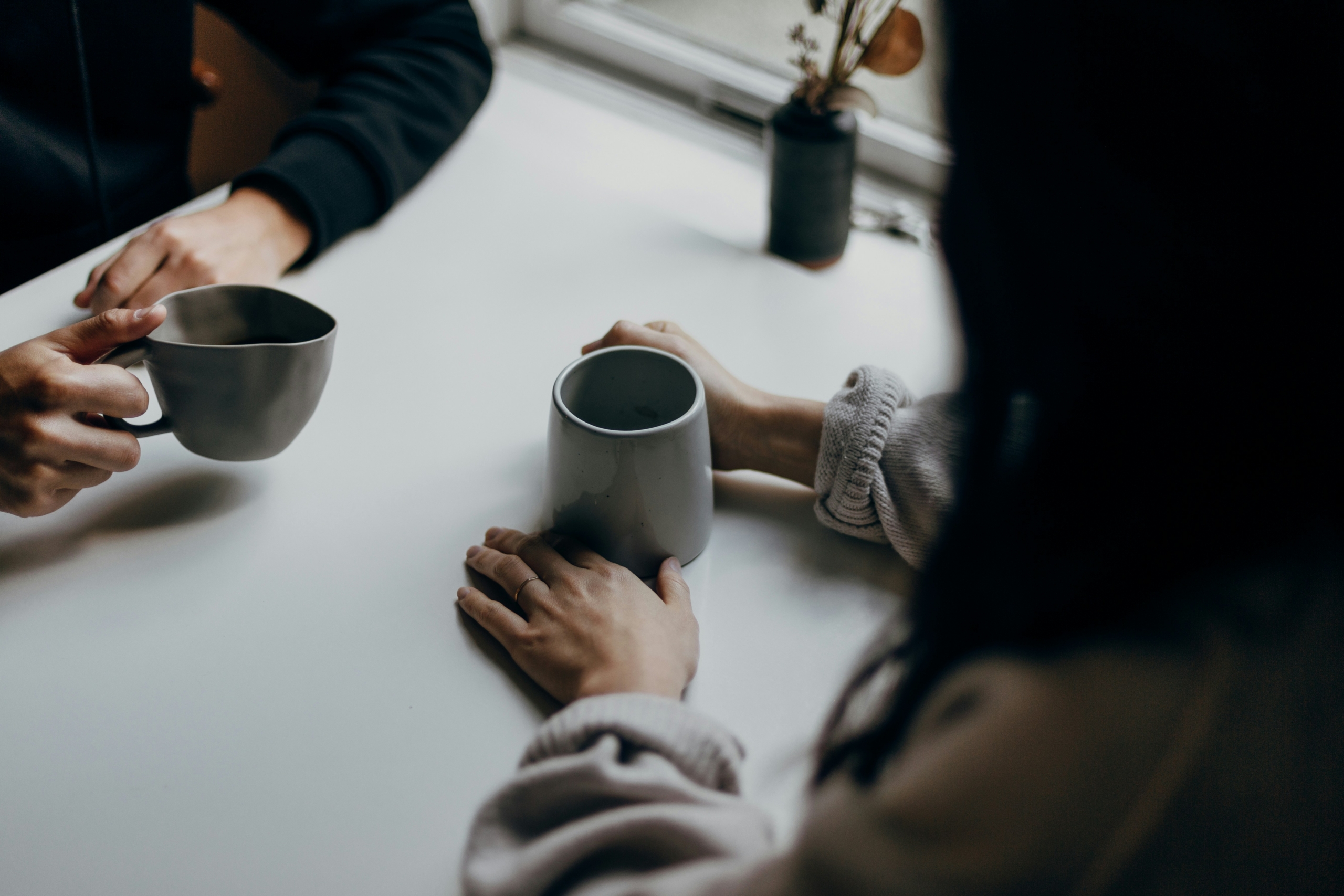 Two people holding mugs across a table during an honest conversation